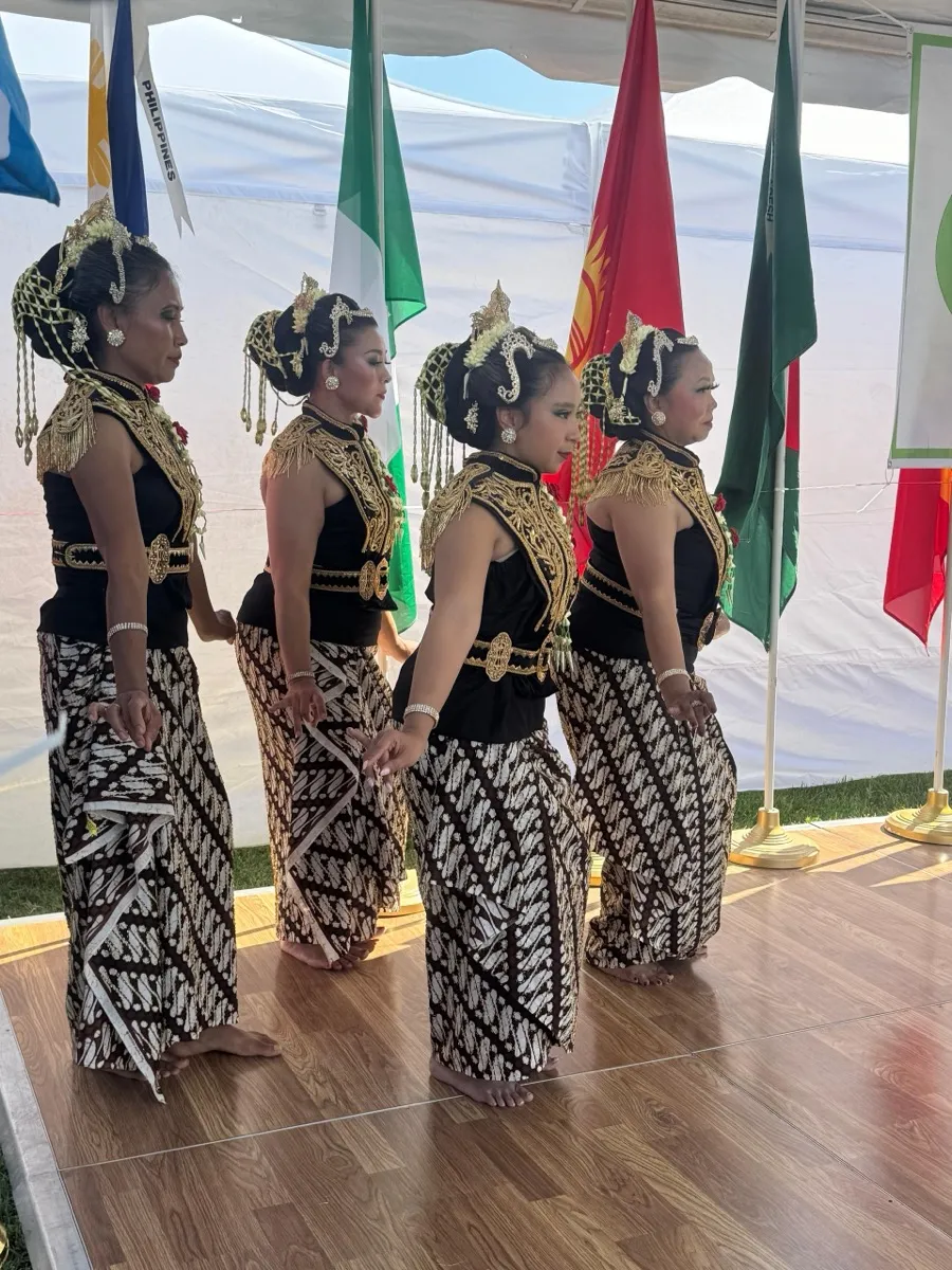 Four dancers in black-and-gold costumes and batik skirts performing on an outdoor stage
